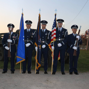 Four veterans associated with the American Comrades team stand in uniform with flags.